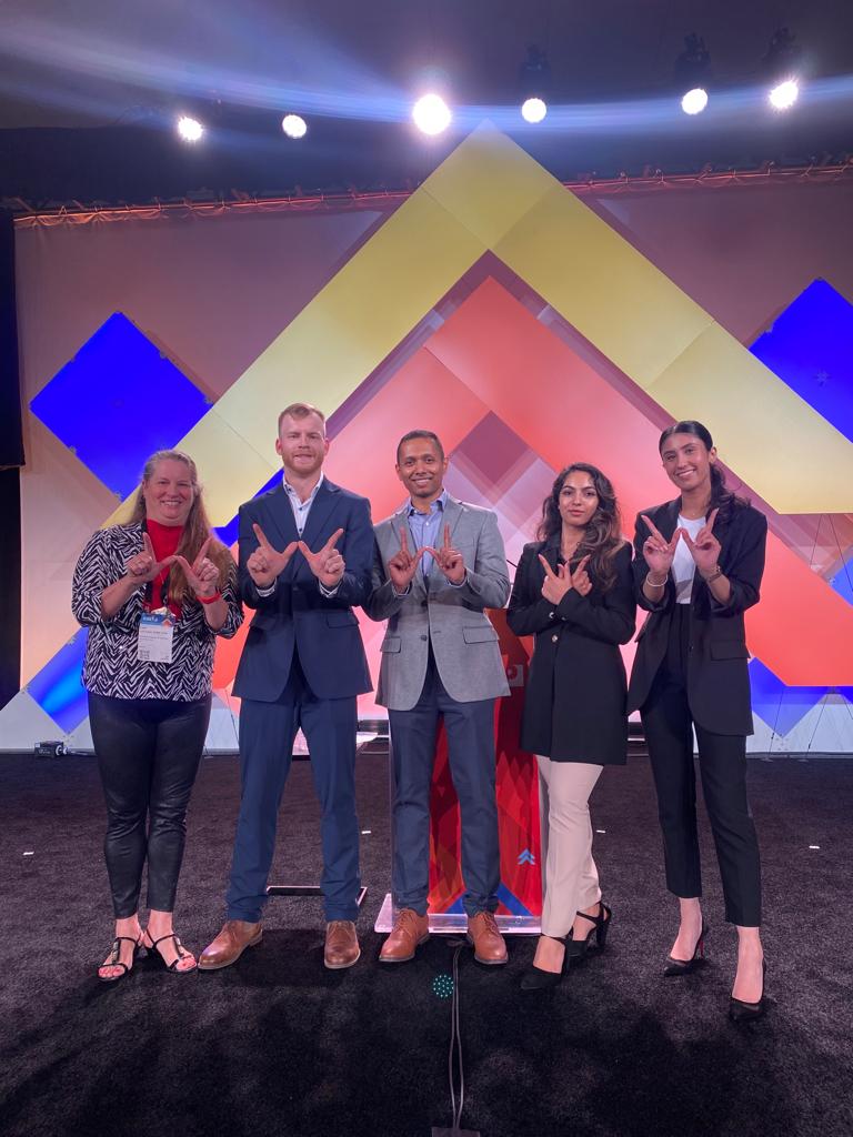 Five people on stage holding their hands to make a W sign