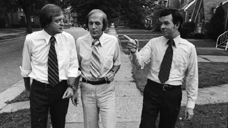 Dennis Hertel, Curtis Hertel and John Hertel walk on a city street.