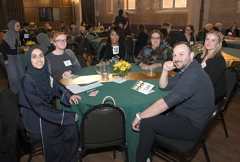  A group of six people sitting around a round table with a green table cloth, smiling at the camera during the 2024 College of Nursing Scholarship Reception.