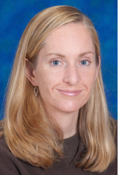 A headshot of faculty member Deborah Charbonneau. She has long blonde hair and is wearing a dark brown sweater against a blue background. 