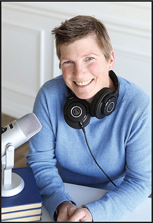 SIS alumna Amy Hermon is pictured behind a microphone with headphones draped around her neck. She has short hair and is smiling at the camera.