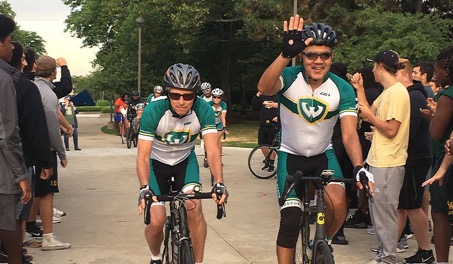 Two Wayne State University cyclists riding through a crowd with several bikers behi