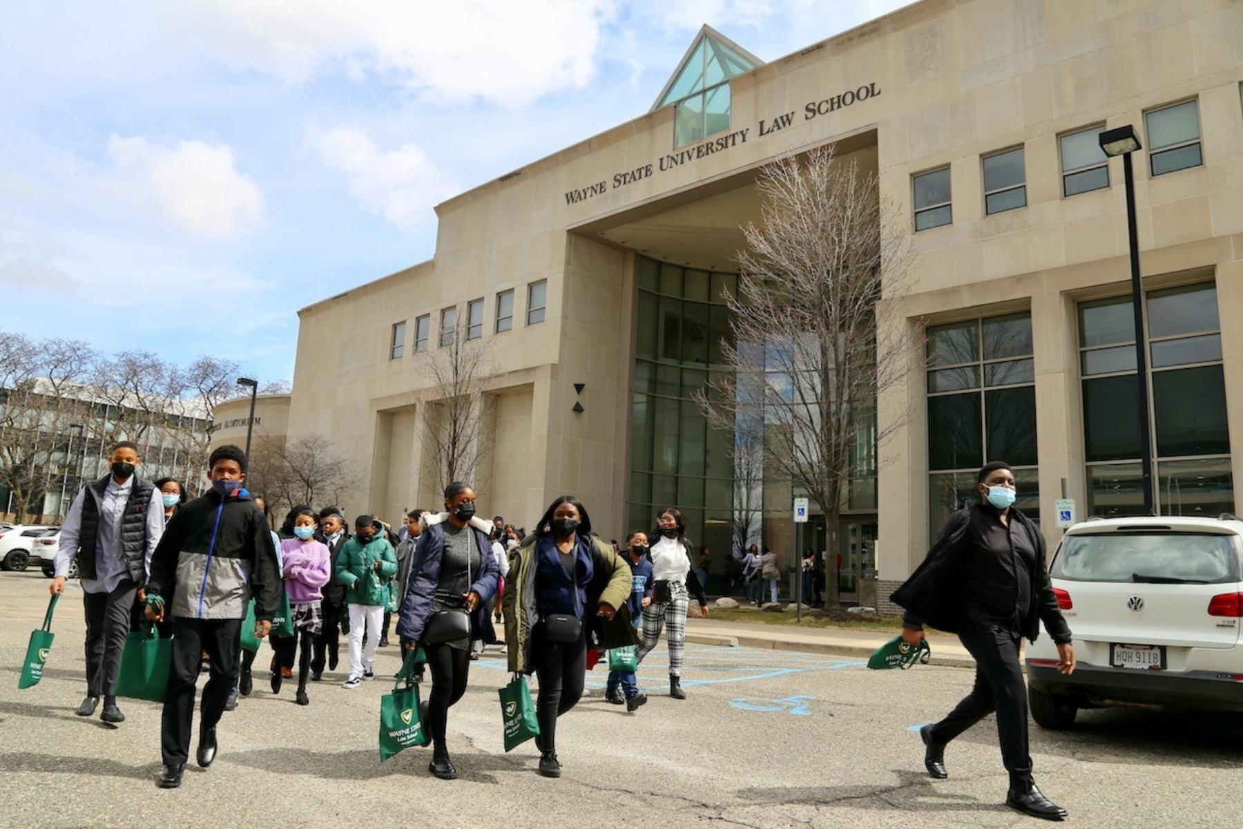 A group of students from the David Ellis Academy walk in the parking lot outside Wayne State University Law School with the building and sign in the background