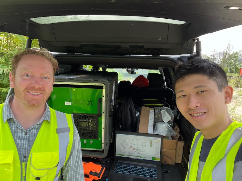 O'Leary and Tay stand in front of back of a van with field equipment in neon safety vests