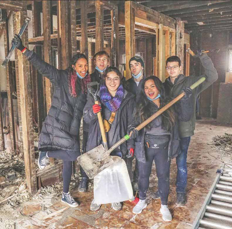 Six Wayne State students hold shovels and cleaning supplies as they clear out and clean up a building. 