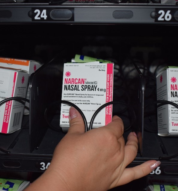 A hand taking a box of Narcan out of a vending machine