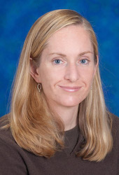 A headshot of Charbonneau, who has medium length blonde hair, pictured against a blue backdrop.