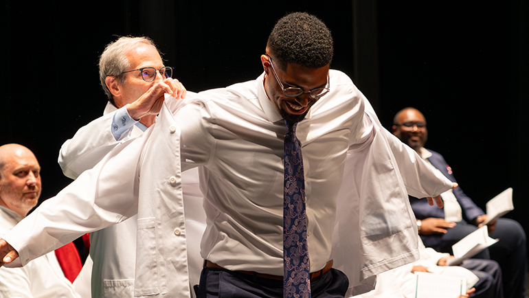 A young man receives his coat during Wayne  State's White Coat ceremony for the Class of 2027, held on July 28, 2023 at the Detroit Opera House.