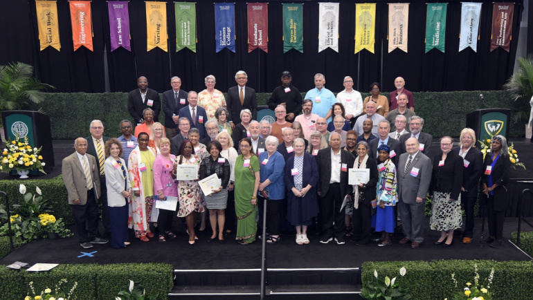 A large group of Wayne State retirees stand on the stage of the Employee Recognition Ceremony at the Wayne State Fieldhouse.