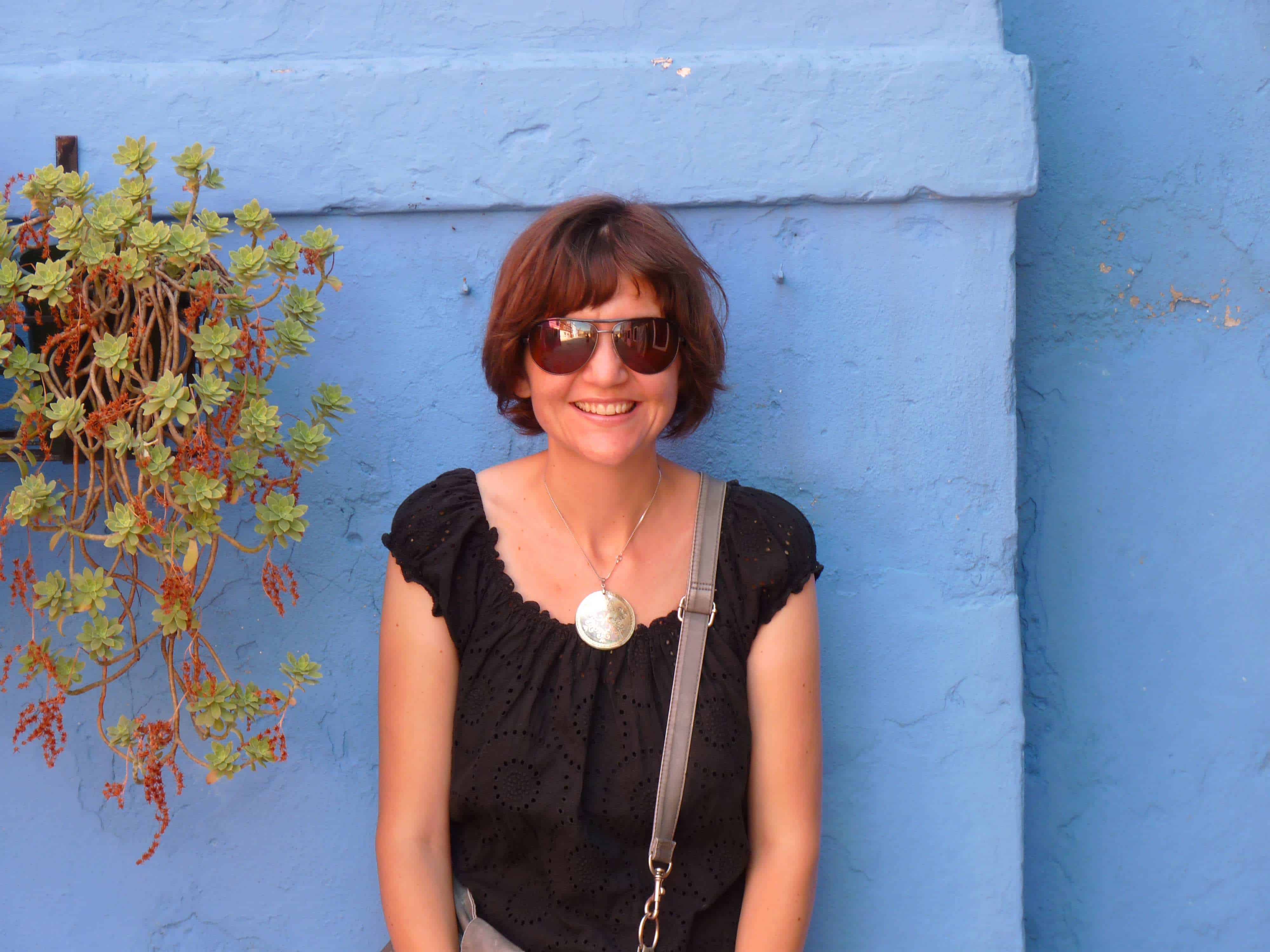 Woman in a black shirt leans against a blue building 