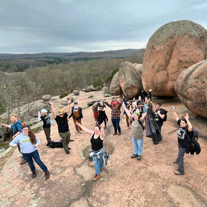 Students with hands up in front of boulders