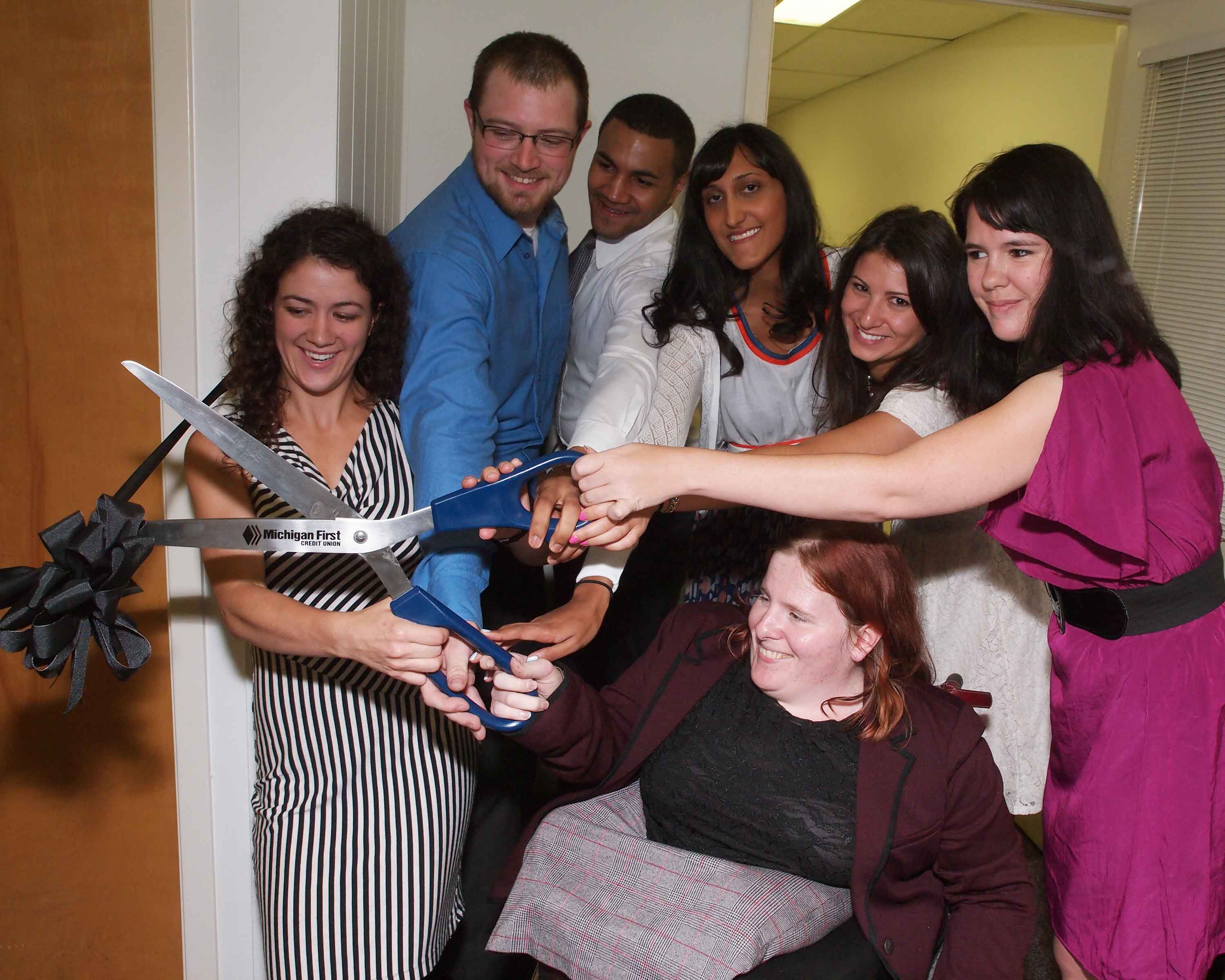 Group of people cutting a ribbon with large scissors