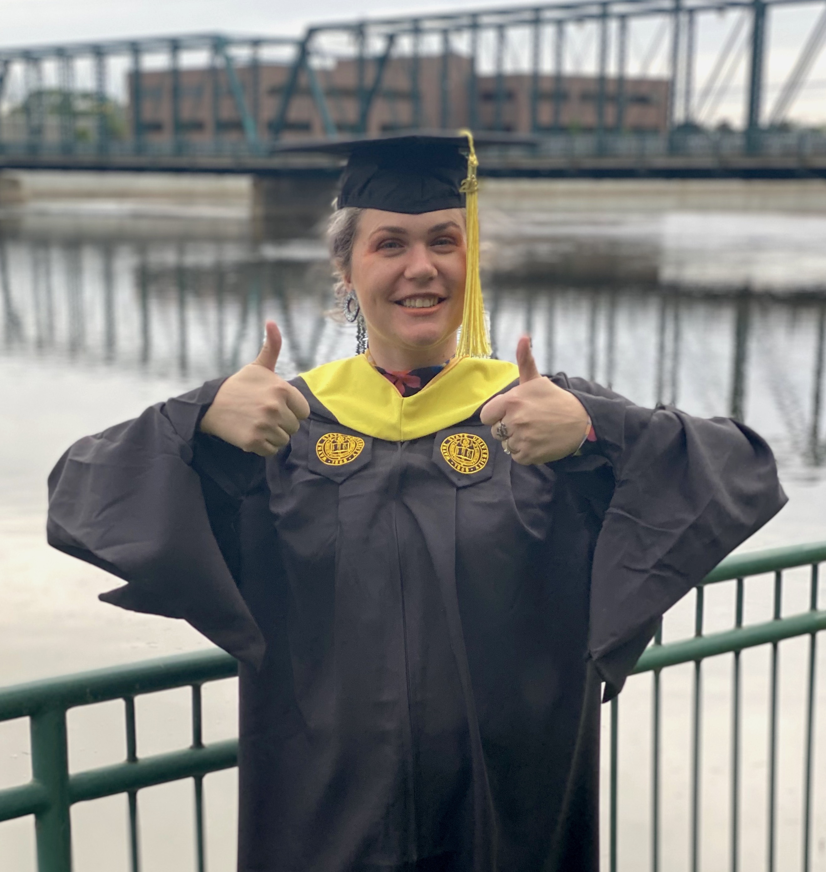 WSU alumna Ginny Schneider is pictured in her graduation cap and gown giving a big smile and thumbs up to the camera.