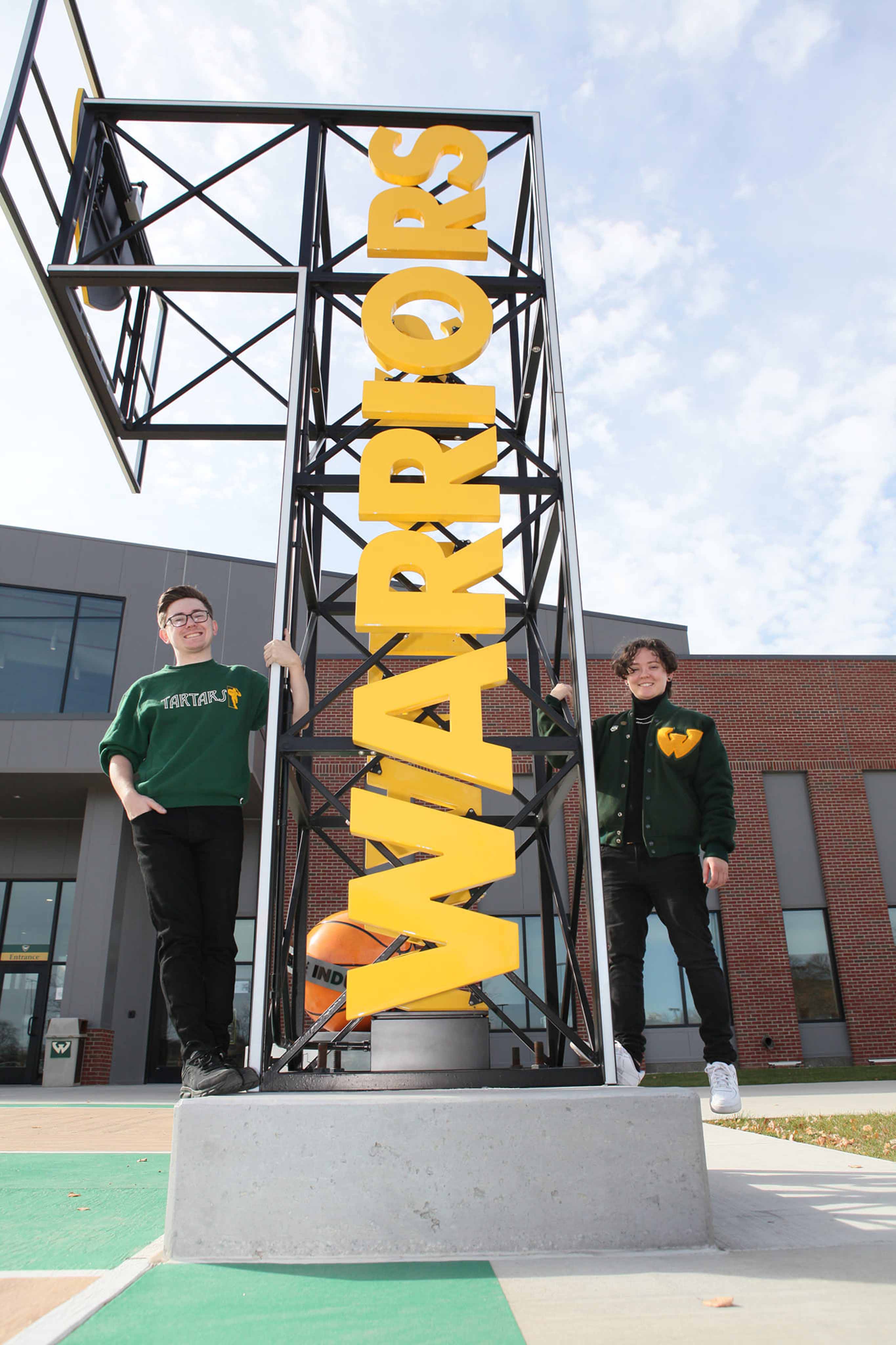 Haley and their brother standing by the big gold WARRIORS sign on Wayne State's campus.