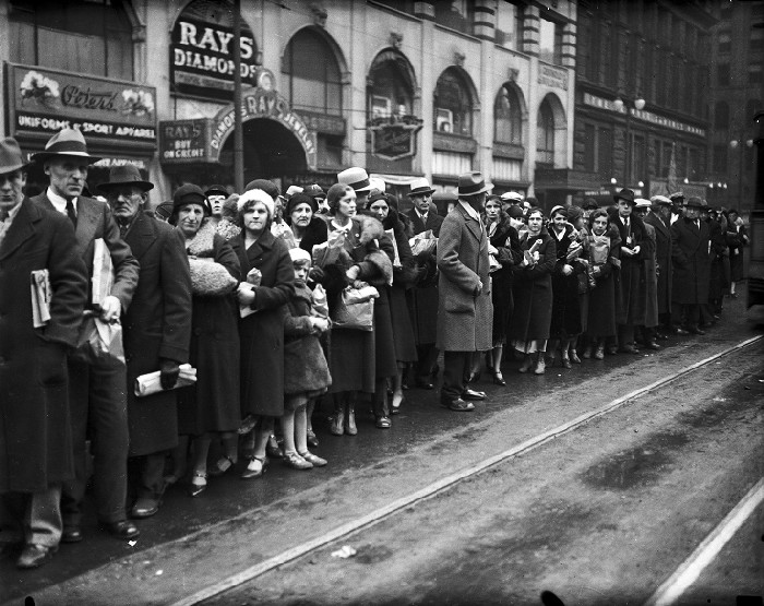 Men and women packed together bundled in their winter coats waiting outside shops