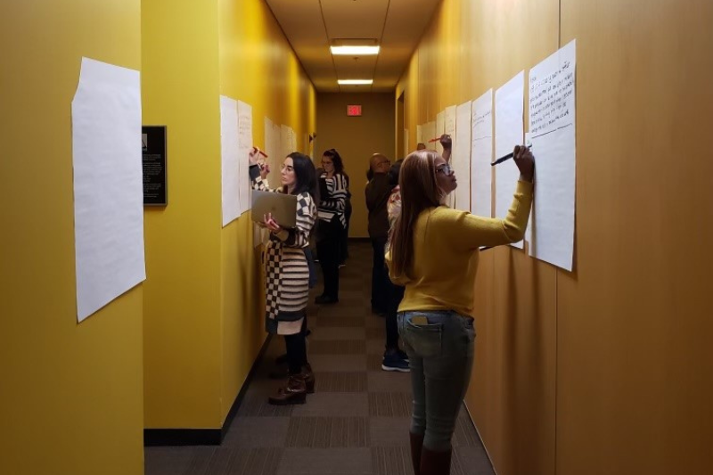 Several people write on large sheets of paper that are taped on walls