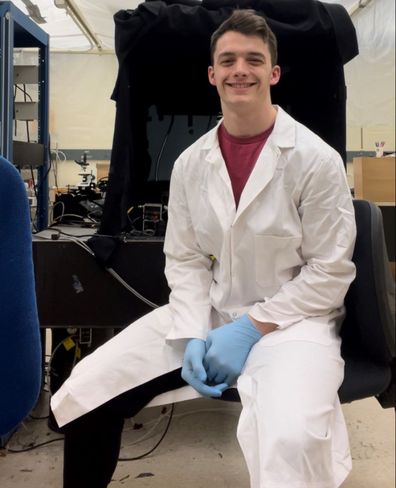 Justin Nelson sits in a lab with a white lab coat on.