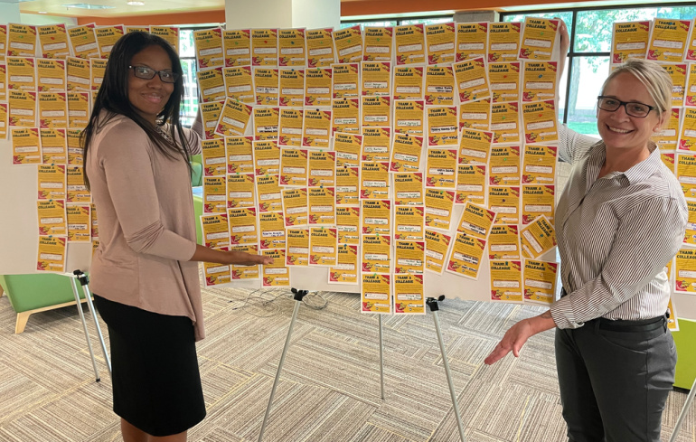 Human Resources employees Mytheia Thomas (left) and Amber Reagan pose next to Thank a Colleague display board in the Student Center.