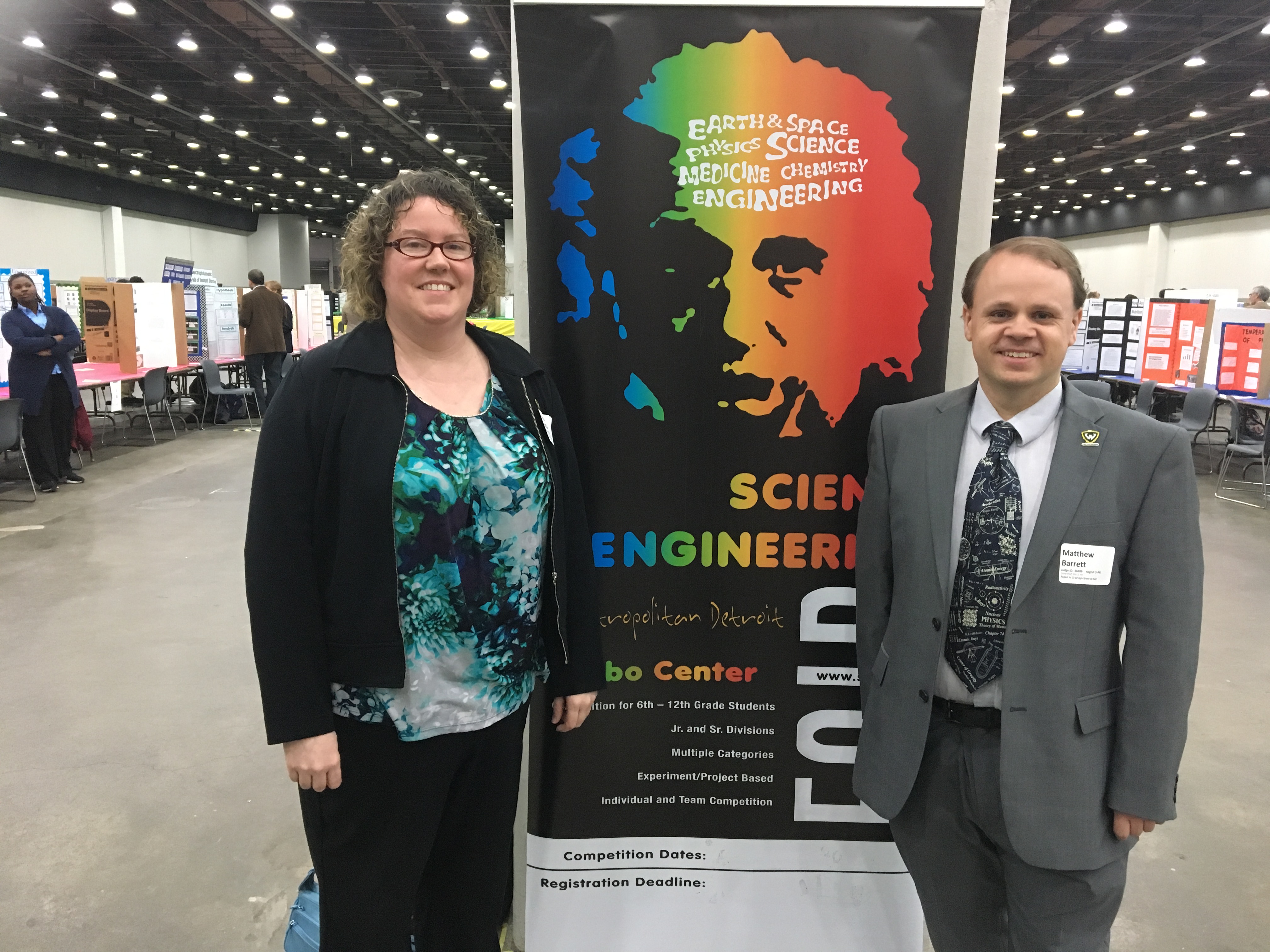 Megan McCullen and Matthew Barrett stand with the banner for the Science Fair, a rainbow colored image of Albert Einstein