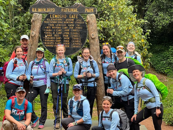 Members of the Kidney Donor Athlete organization, sporting climbing gear and matching shirts, are pictured in front of a sign for Mount Kilimanjaro’s Lemosho Gate. 