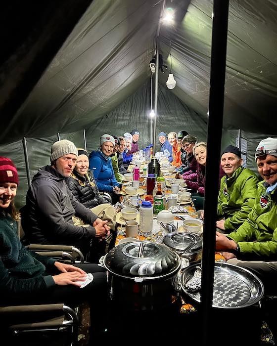 Emily and her fellow climbers are seated at a long table in a tent, ready to eat a meal together at basecamp.