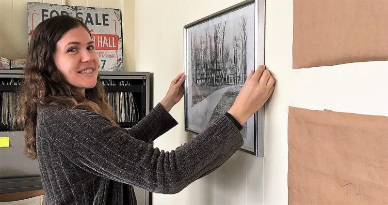 Ginny Schneider smiles toward the camera while hanging a historic photo on the wall of the office she helped redesign.