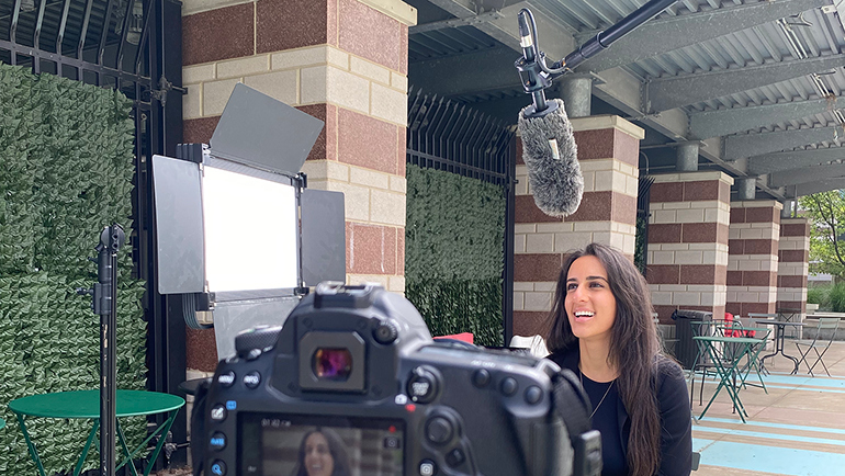 Wayne State University alumna and 2018 recipient of the Mike Ilitch School of Business Emerging Business Leader Award Lydia Michael outside sitting in a chair doing a video recording