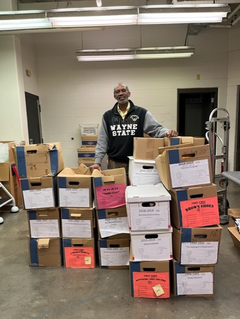 Jones is pictured wearing a Wayne State sweatshirt and is standing behind several boxes of archival materials.