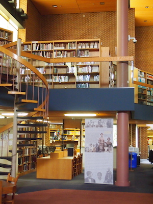 An interior image from the Maryland State Archives showing a spiral staircase and several shelves filled with books.