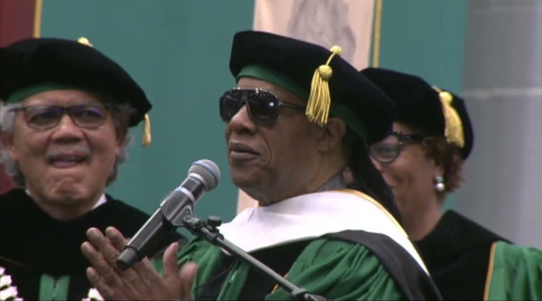 Stevie Wonder talks into a microphone at commencement.