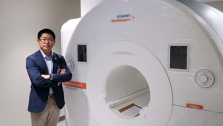 Yongsheng Chen, Ph.D., associate professor of neurology and director of the MR Research Facility, stands next to the Siemens 3T MAGNETOM Cima.X scanner inside the Eugene Applebaum College of Pharmacy and Health Sciences.