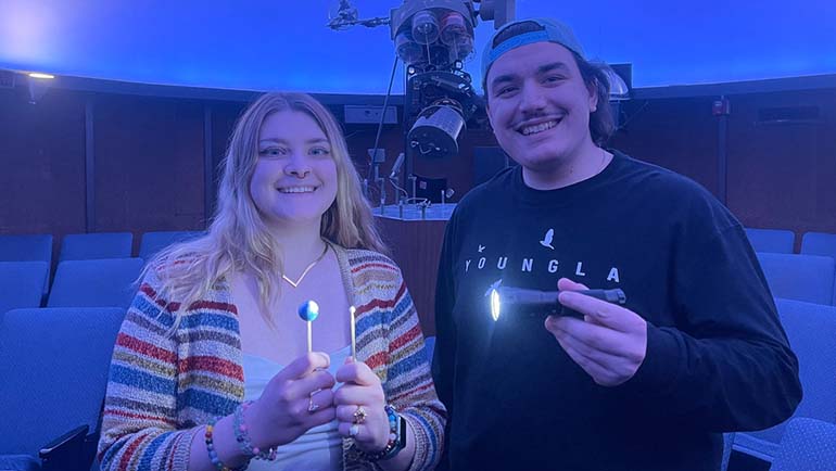 Two Dead Stars Society students holding a model of the total solar eclipse - they served as NASA eclipse ambassadors giving presentations in the Henry Ford planetarium and local libraries.