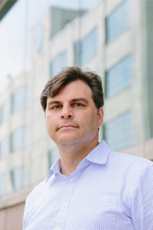 A headshot of a man standing outside an office building