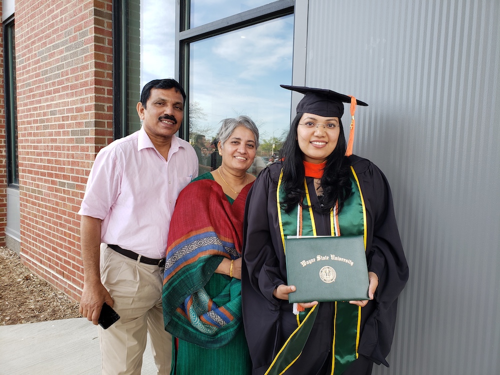 WSU Engineering graduate with her parents at commencement, smiling, wearing regalia and holding her diploma.