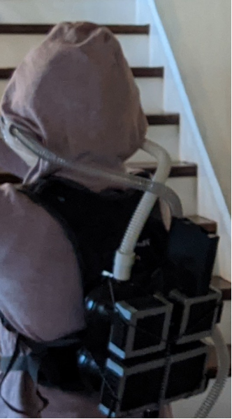Back view showing device mounted on backpack and CPAP hoses connecting to the hood