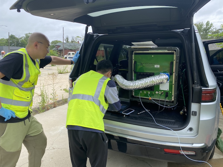 Two people in neon vests working on field equipment in back of van