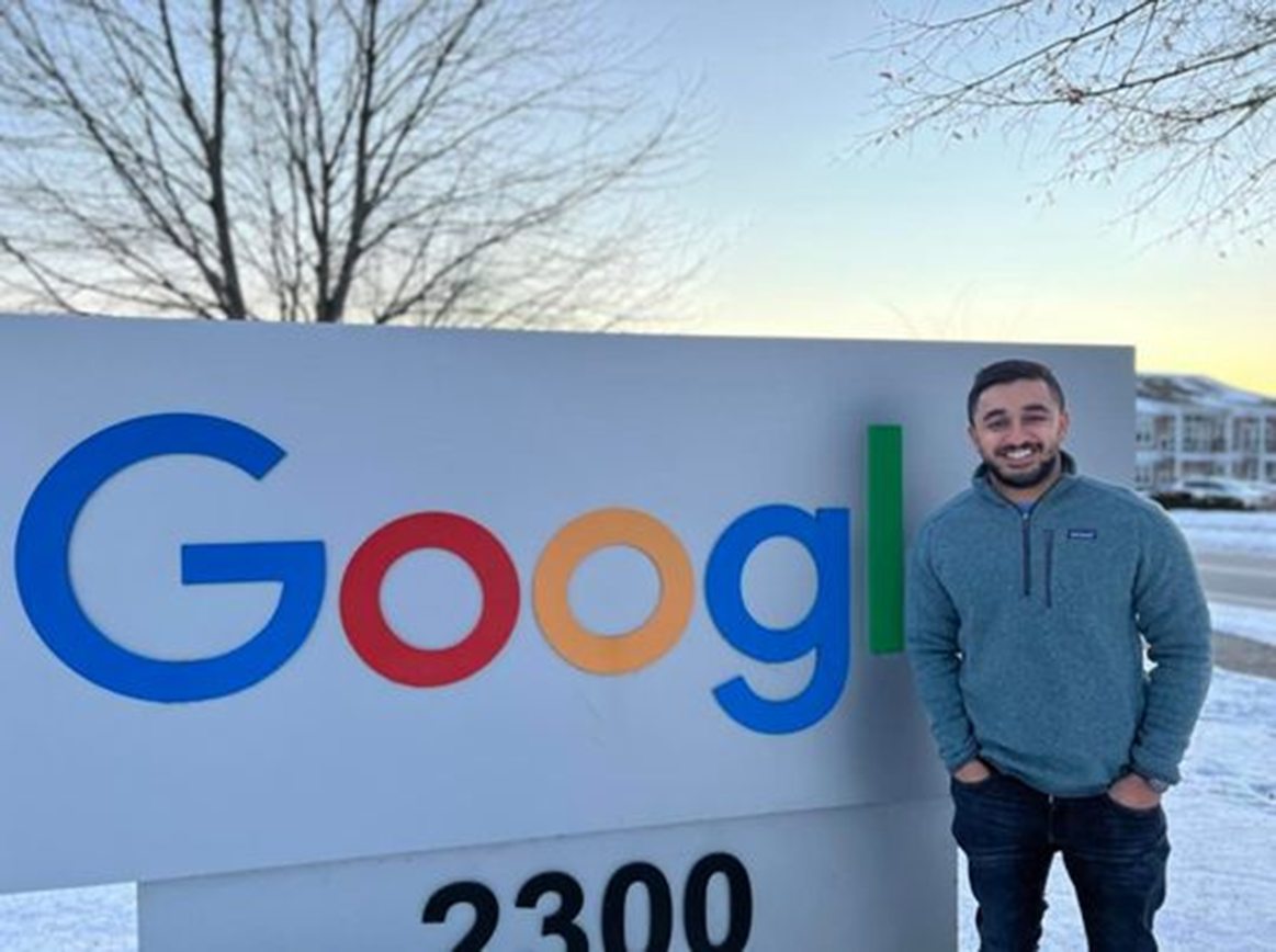 Wayne State graduate standing outside in the winter in front of the Google sign.