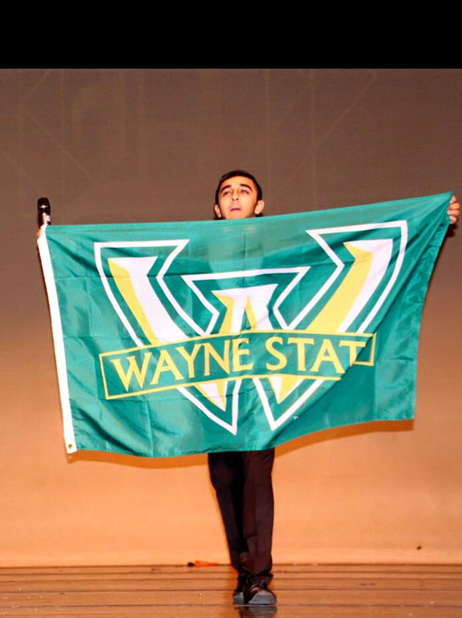 Wayne State student standing on stage, holding a green, white and gold Wayne State flag.