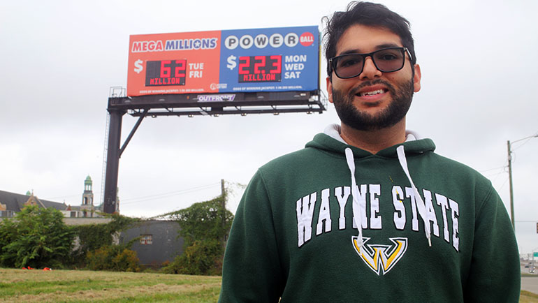 Shawzub Raza stands in front of a Powerball lottery billboard off of the I-94 freeway in Detroit.