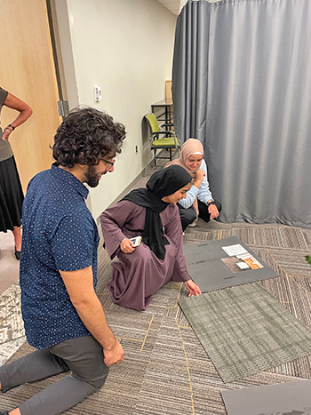 Three Wayne State students in the old Reflection Room, looking at samples of new carpet options, smiling and kneeling on the floor.