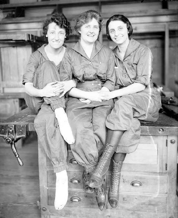 Three smiling women sitting on top of a work bench