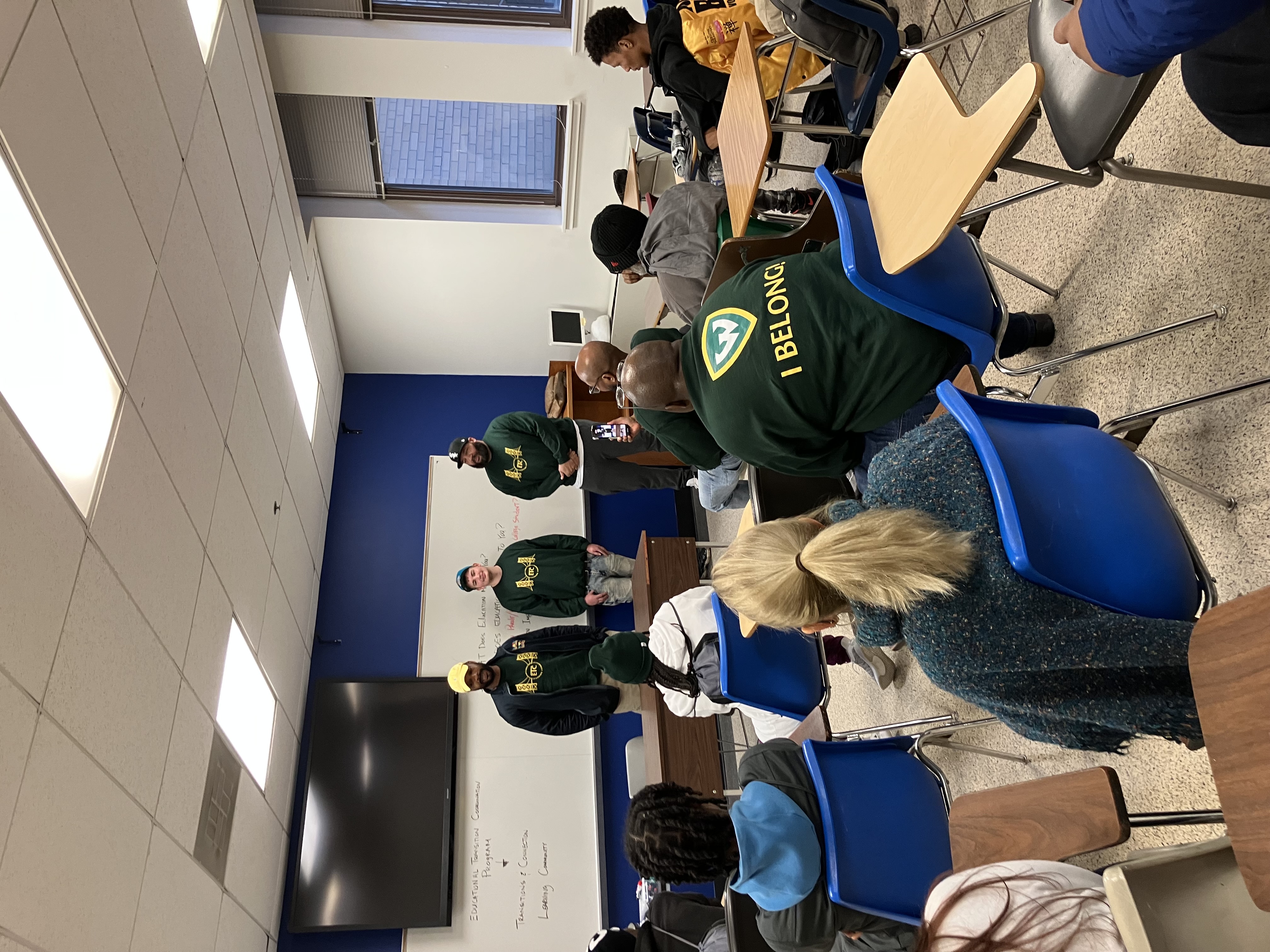 Three men stand at the front of a classroom of students