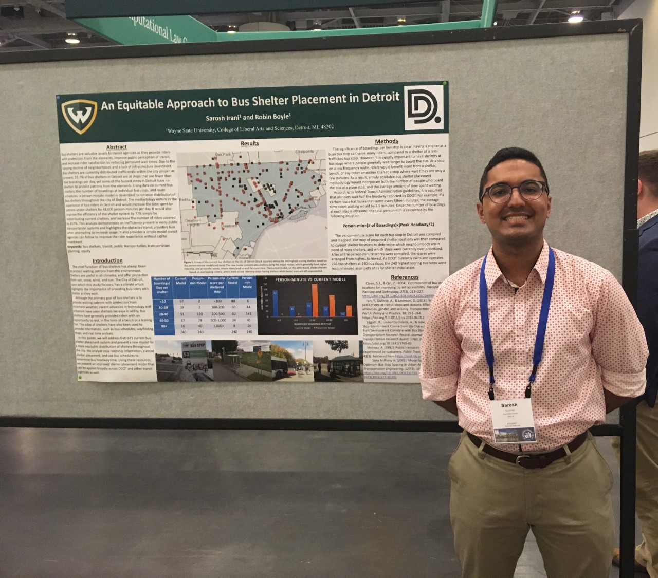 Sarosh Irani standing in front of gray display stand smiling with his research poster next to him
