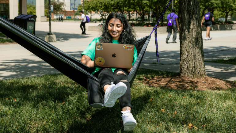 A student works on her laptop sitting on campus.