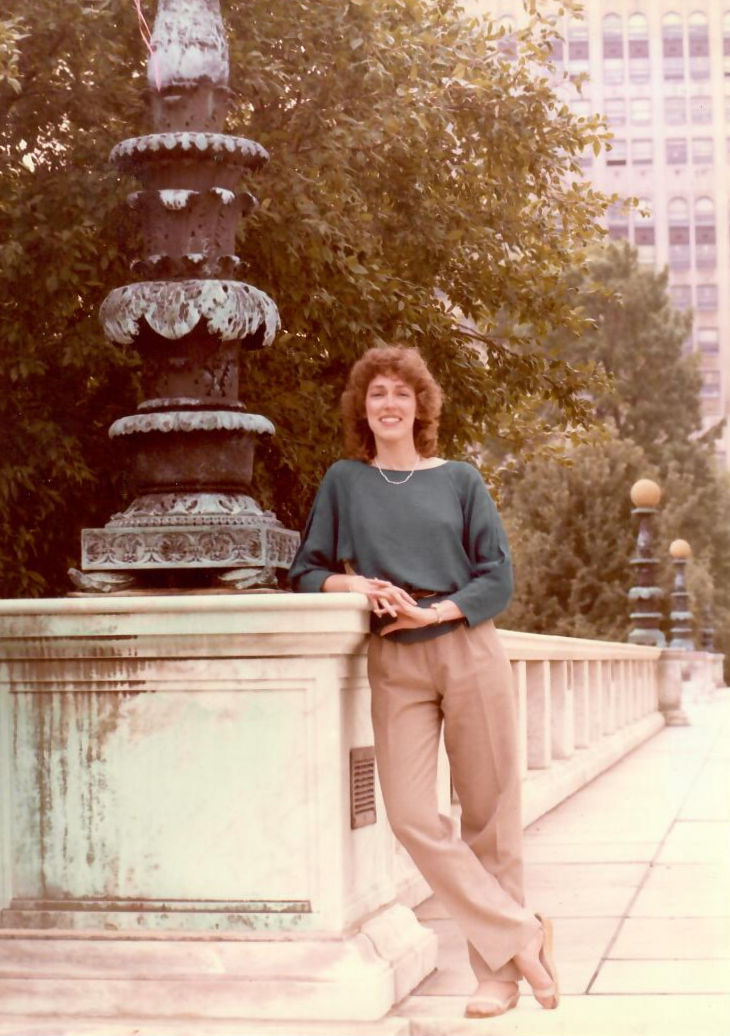 School of Information Sciences alumna Martha Sneed is pictured in front of a stone walkway outside of the Detroit Institute of Arts in 1982. She is wearing a sage green top and khaki pants and is leaning with her elbow on the railing.