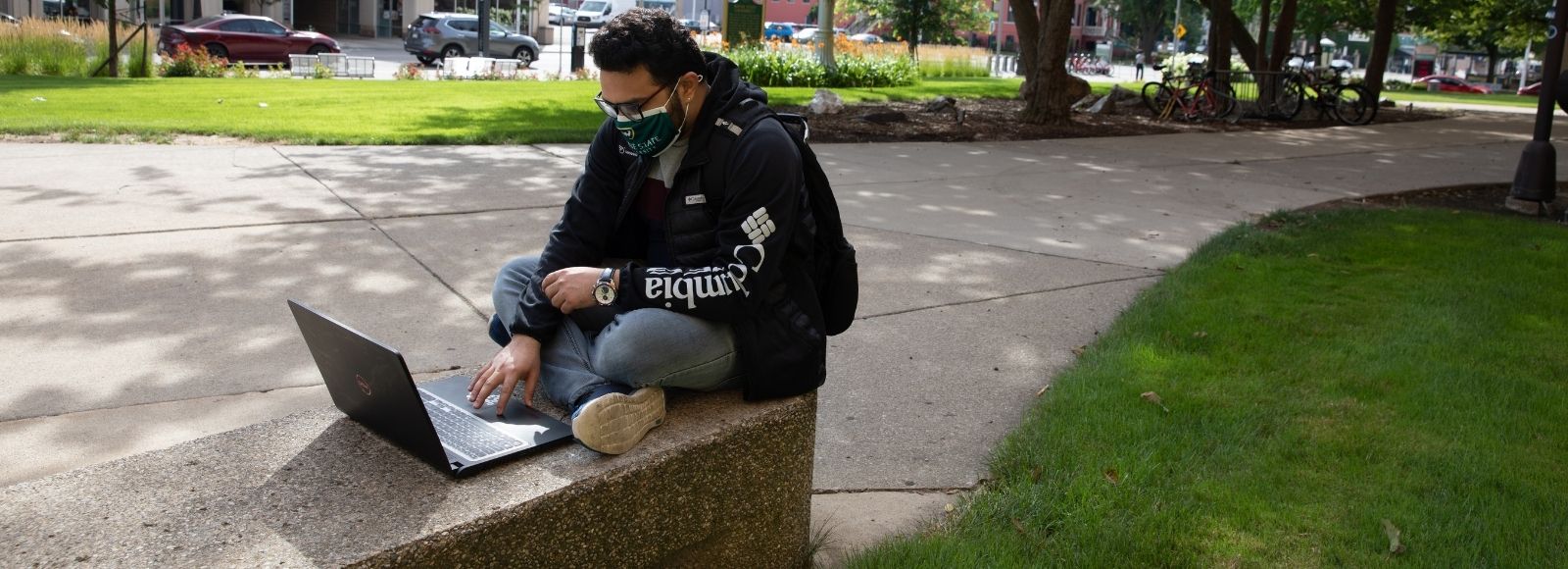 Student sitting in front of laptop outside of Old Main.