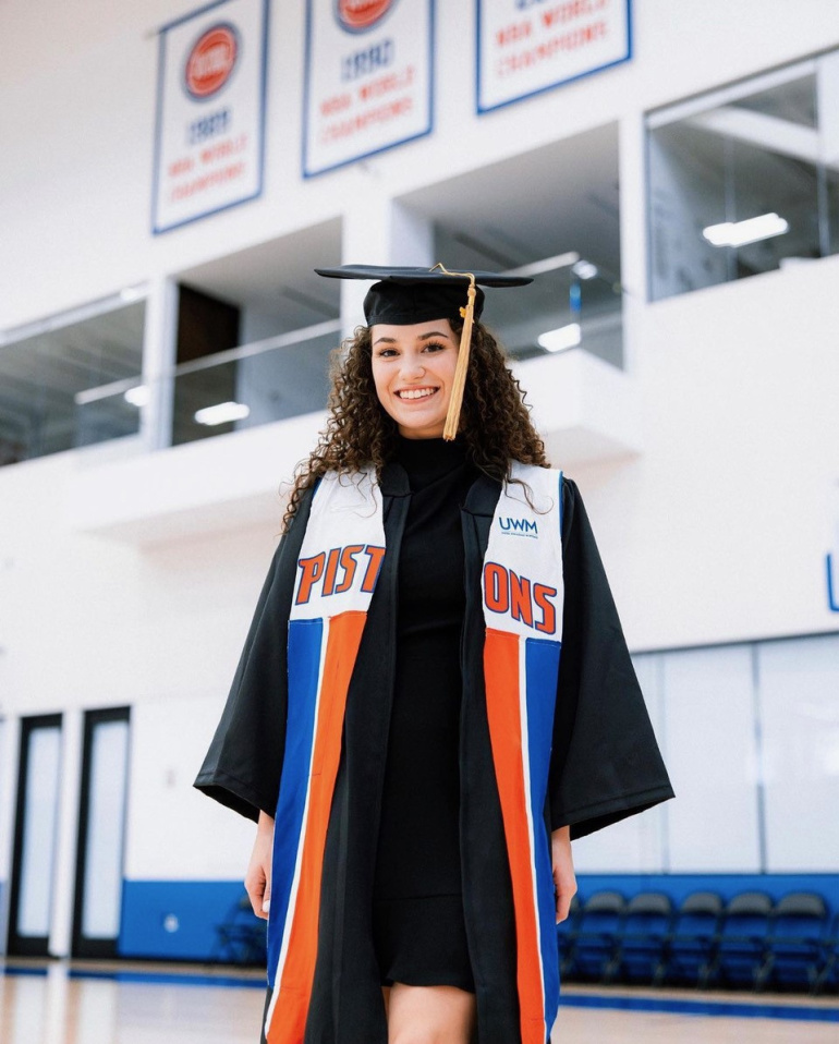 Jenae Lodewyk poses for a photo in her Wayne State cap and gown at the Pistons' practice facility.
