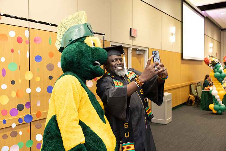 A graduate takes a selfie with Wayne State University W mascot at the 2024 Rainbow Graduation and Homecoming.