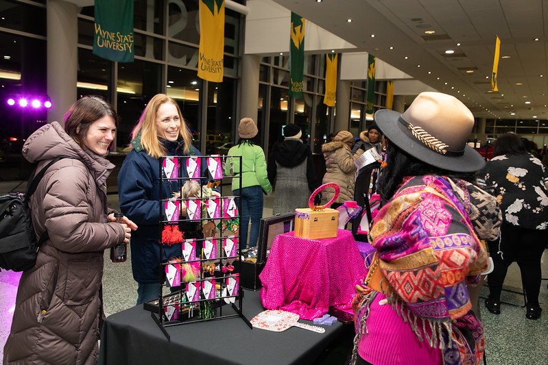  Two people smiling and chatting with a small business owner that is standing behind a table display of accessories